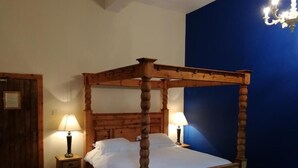 Un lit à baldaquin avec une structure en bois et un couvre-lit blanc, flanqué de deux tables de chevet avec des lampes, dans une pièce aux murs bleus et à la porte en bois.