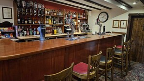 Un espace bar avec des chaises en bois, un comptoir doté d’une tireuse à bière Guinness, des étagères remplies de bouteilles d’alcool et une horloge au mur.