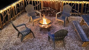 An outdoor seating area with Adirondack chairs and a central fire pit, surrounded by a wooden fence and string lights. - Knotty Pine cabin, Couples Retreat w/ Hot Tub
And Patio Gas log Fireplace. (Jasper)