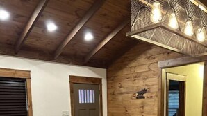 A cozy room with a wooden ceiling, a large wooden dining table, two leather armchairs, a small side table, and a decorative wall piece. - Knotty Pine cabin, Couples Retreat w/ Hot Tub
And Patio Gas log Fireplace. (Jasper)