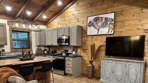 A modern kitchen with grey cabinets, a stainless steel range, and a large flat-screen TV. - Knotty Pine cabin, Couples Retreat w/ Hot Tub
And Patio Gas log Fireplace. (Jasper)