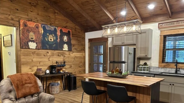 A cozy cabin interior with a wooden ceiling, a bar area with stools, a leather sofa, and a bear-themed artwork on the wall. - Knotty Pine cabin, Couples Retreat w/ Hot Tub
And Patio Gas log Fireplace. (Jasper)