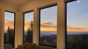 Un saló modern amb grans finestres que ofereixen una vista d'un bosc i muntanyes durant el capvespre.
