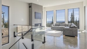 Zona d'estar àmplia amb un disseny modern, que destaca per una escala de vidre, un sofà gràveu gran i una llar de foc.