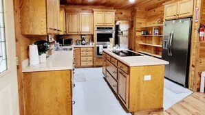 A wooden cabin-style kitchen with wooden cabinets, a stainless steel refrigerator, and a built-in oven. - Spacious log cabin for country getaway (Teague)