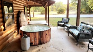 A wooden cabin with a hot tub, wicker furniture, and a covered patio overlooking a grassy area. - Spacious log cabin for country getaway (Teague)