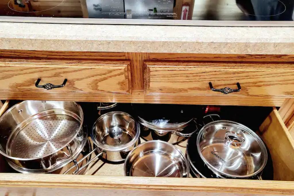 A kitchen drawer with stainless steel cookware including pots and a colander.
