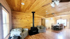 A wooden cabin interior with a fireplace, a sofa, a dining table, and a chandelier. - Spacious log cabin for country getaway (Teague)