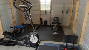Ein Fitnessstudio mit Trainingsgeräten, darunter Laufband, Crosstrainer und eine Gewichtbank.