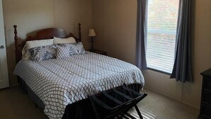 Ein Schlafzimmer mit Bett, Nachttisch, Lampe, einem Fenster mit Vorhängen und einem Sessel.