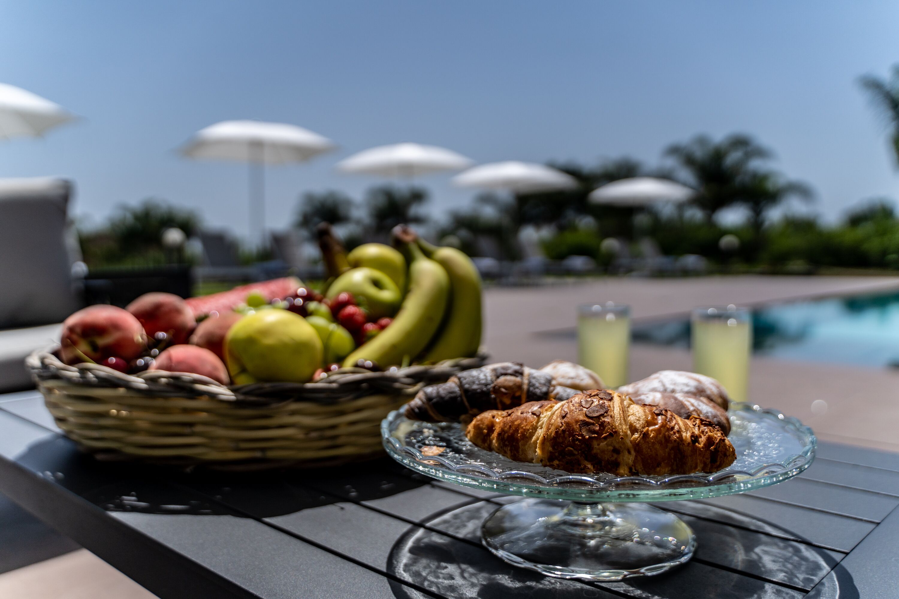 A table with a fruit basket, croissants, and a glass dish.