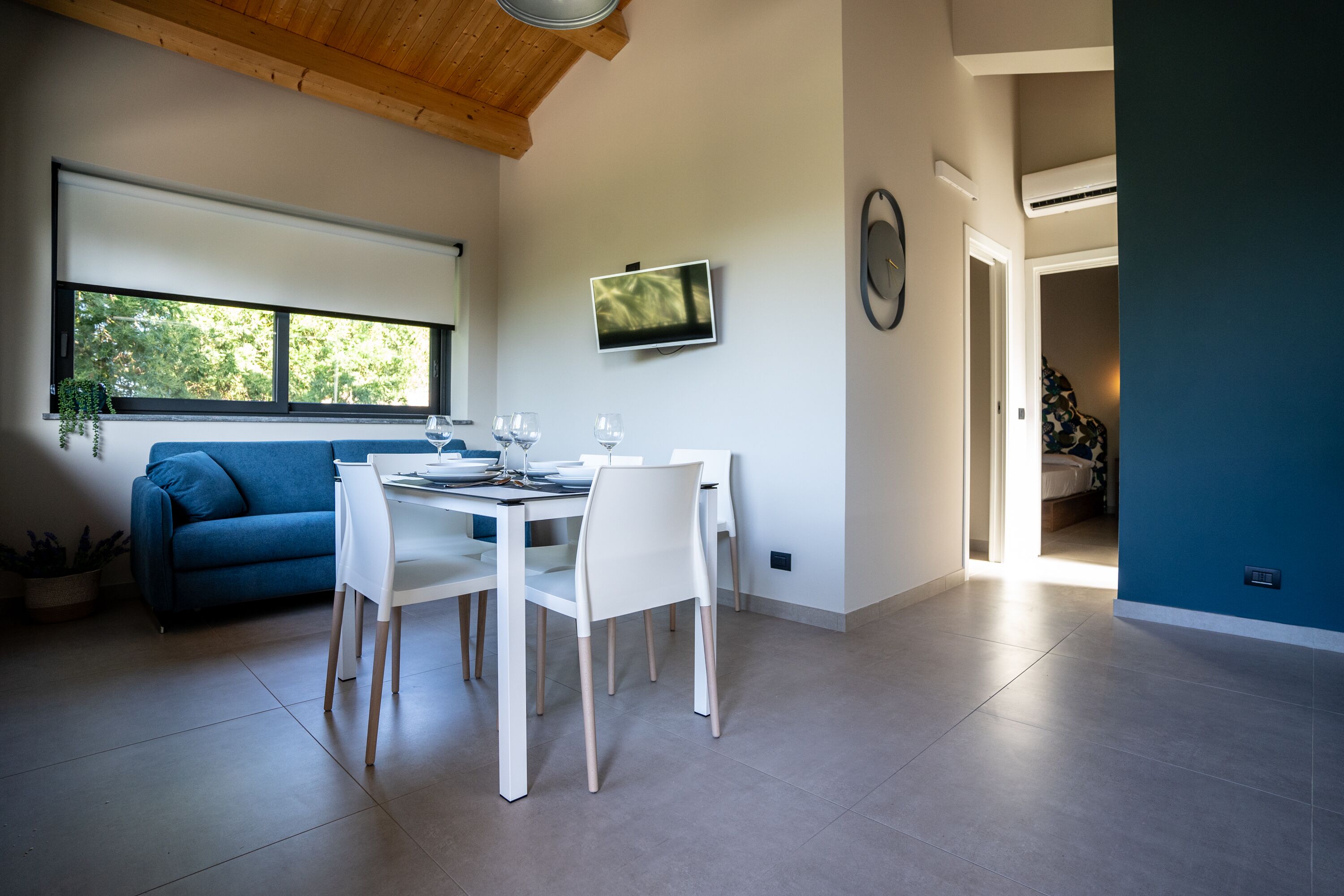 A modern dining area with a white table and chairs, a blue sofa, and a TV mounted on the wall.