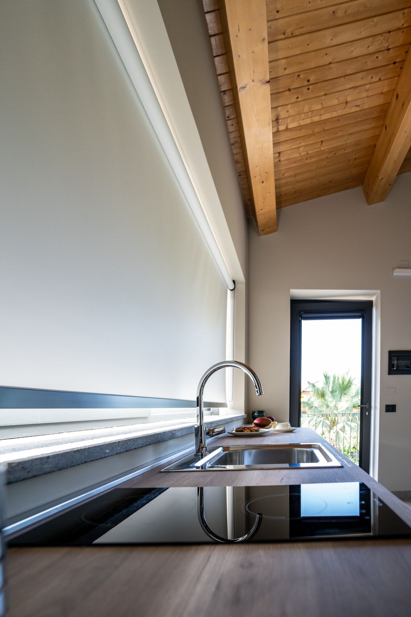 Una cocina moderna con un lavamanos de acero inoxidable, vigas de techo de madera y vistas al exterior.