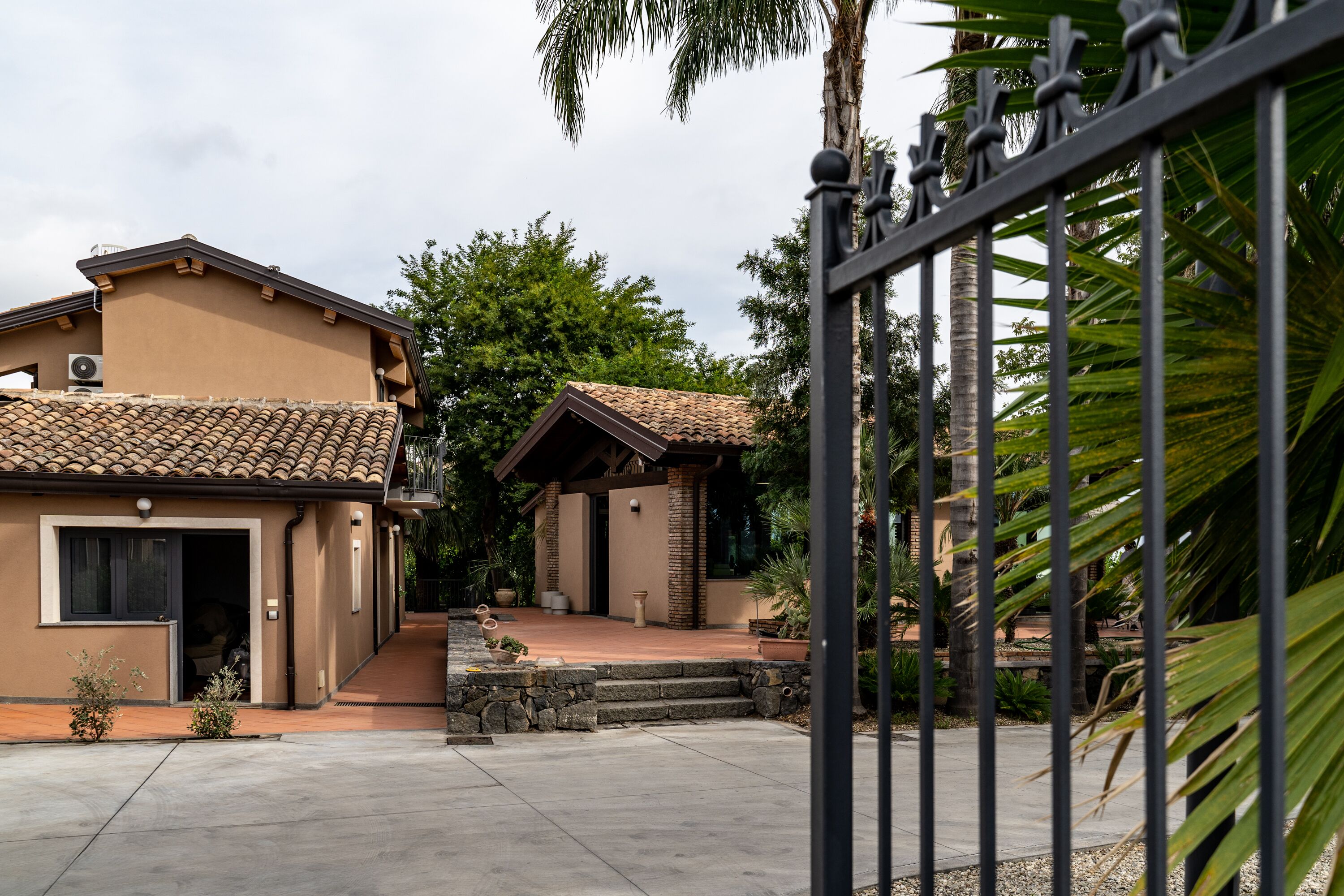 A residential area with two houses, a paved driveway, and a metal gate.