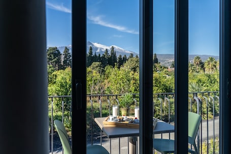 A balcony with a table set for breakfast, overlooking a mountain and lush greenery.