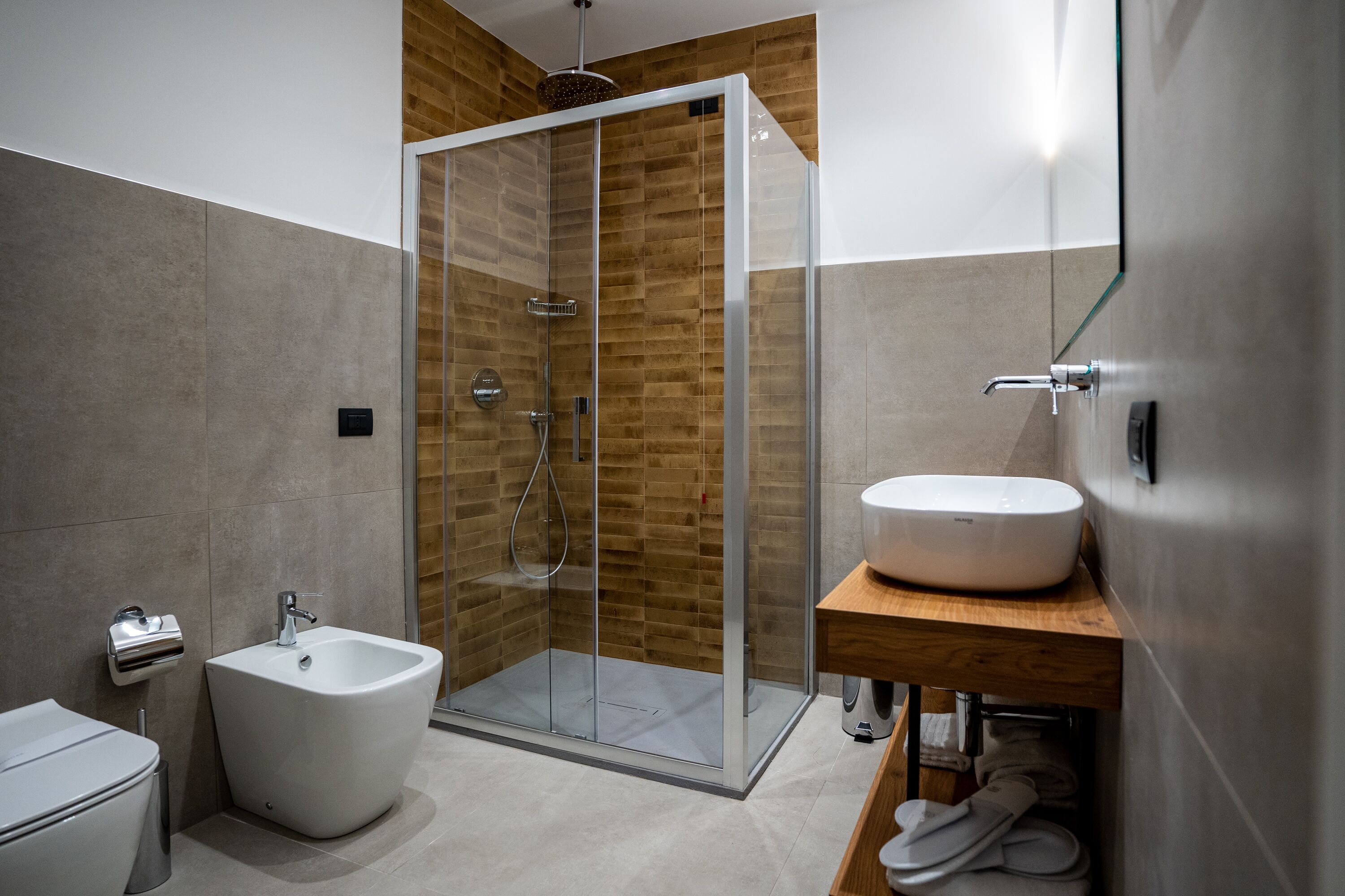 A modern bathroom with a glass-enclosed shower, a white pedestal sink, and a bidet.