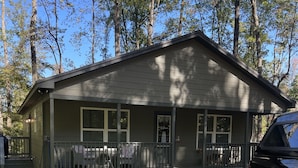 Eine zweistöckige Hütte mit Veranda, einem Willkommensschild und einem kleinen Garten.