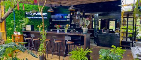 An outdoor bar area with a wooden counter, bar stools, and various plants.