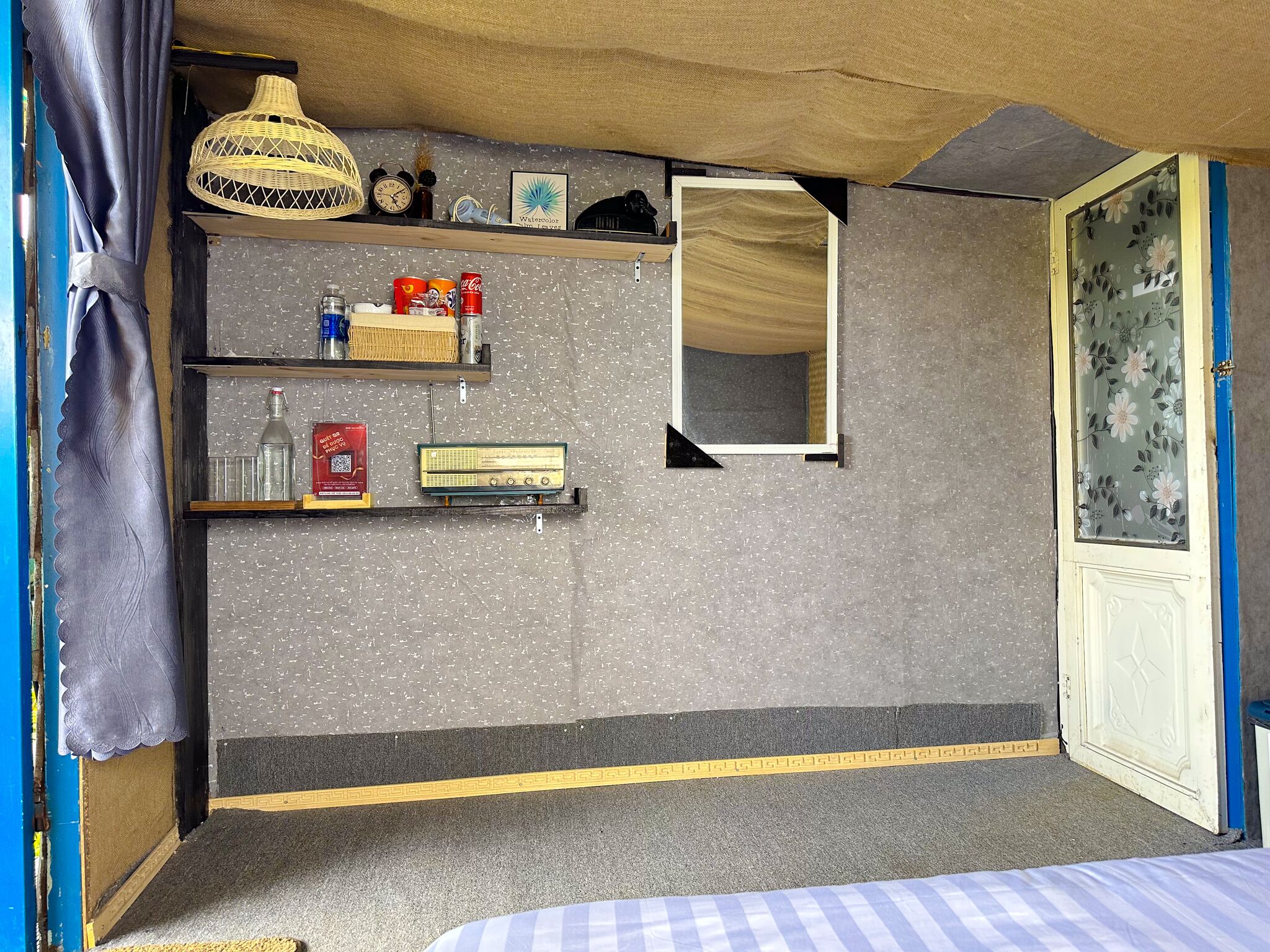 Pieni huone, jossa on sänky, hylly, jossa on hygieniatarvikkeita, radio ja peili.