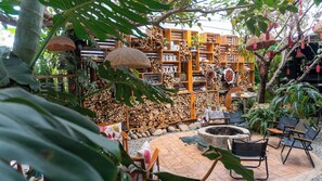 A rustic outdoor seating area with wooden furniture and a fire pit, surrounded by wooden shelves filled with plants and decorative items. - Gio Homestay  (Xuan Huong - Da Lat)