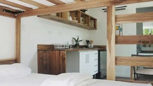 Een slaapkamer met een houten plafond, een bed met wit beddengoed, een klein bureau met een plant en een witte garderobe.