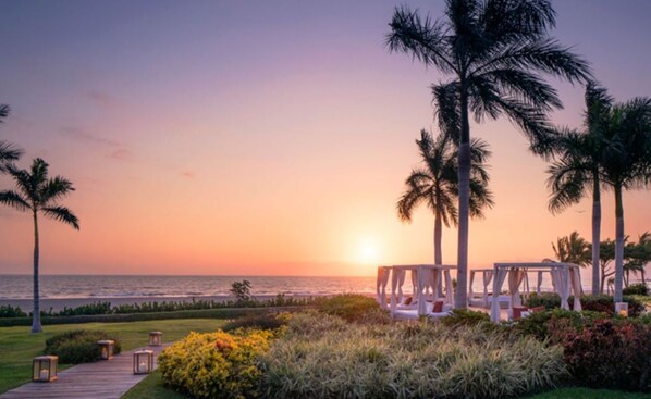 A sunset view with a beach, palm trees, and outdoor seating areas.