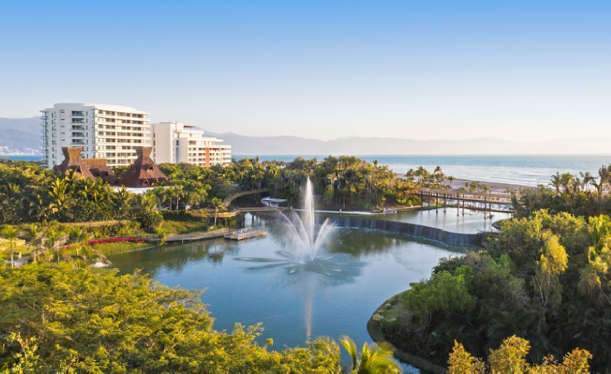 Ein Resort mit einem zentralen Wasserspiel, üppiger Vegetation und Blick auf den Ozean.