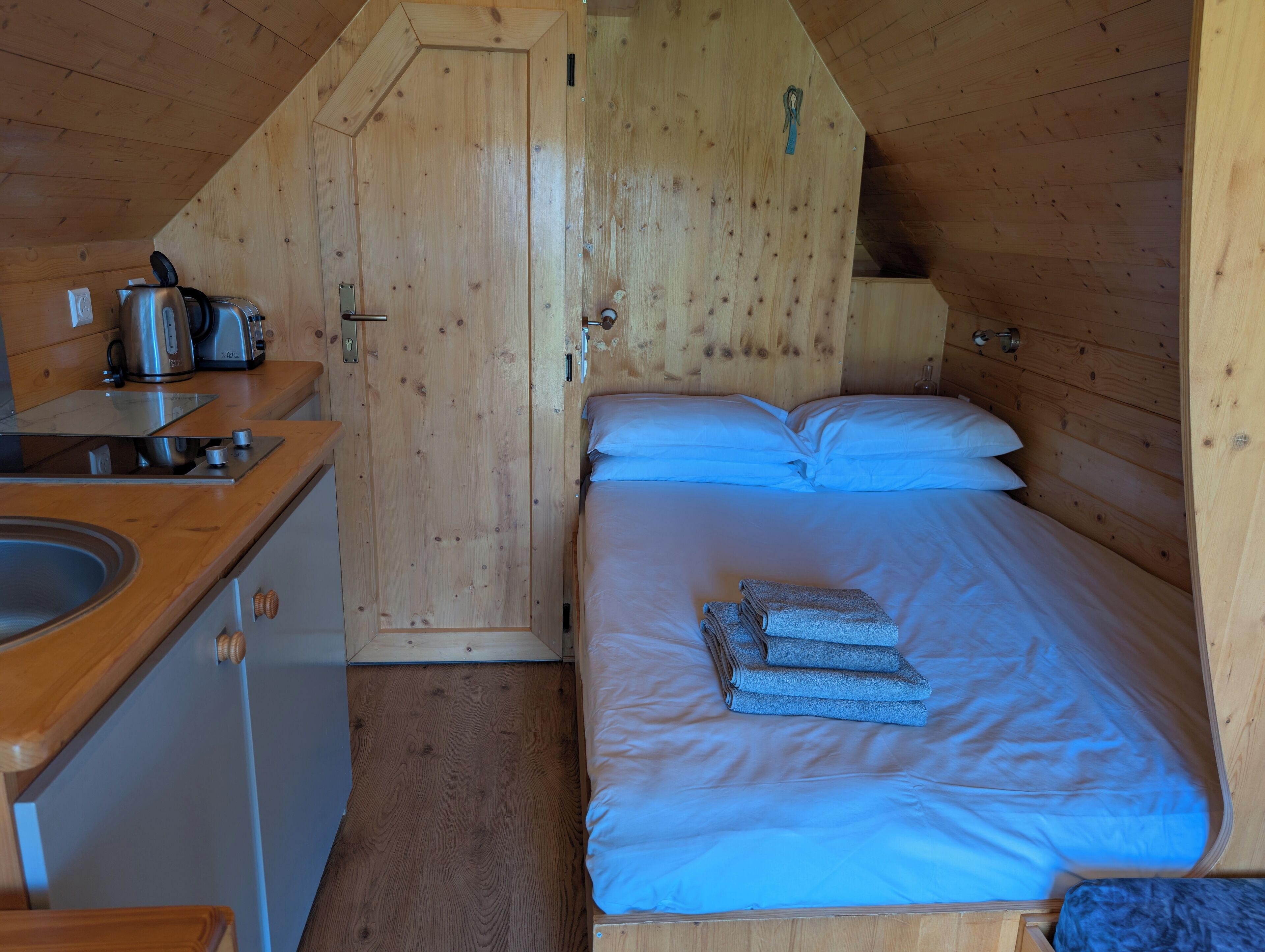 A cozy wooden cabin with a kitchenette, a bed with blue bedding, and a wooden door.