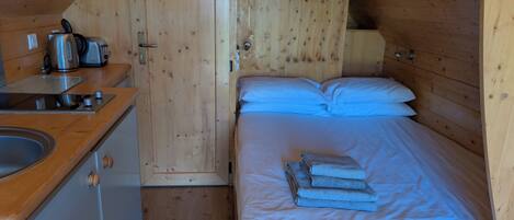 A cozy wooden cabin with a kitchenette, a bed with blue bedding, and a wooden door.