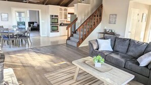 Un vaste espace de vie comprenant une table basse en bois, un canapé gris et un escalier menant à un niveau supérieur.