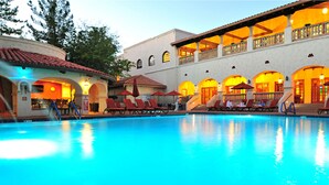 A swimming pool with lounge chairs and umbrellas, surrounded by buildings with arched windows and balconies.