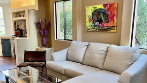 A living room with a sectional sofa, a glass coffee table, a cowhide rug, a purple vase, and a painting of a bull. - Charming Adobe Casita! Large lot in upscale quiet neighborhood. STR 15734641 (Fountain Hills)