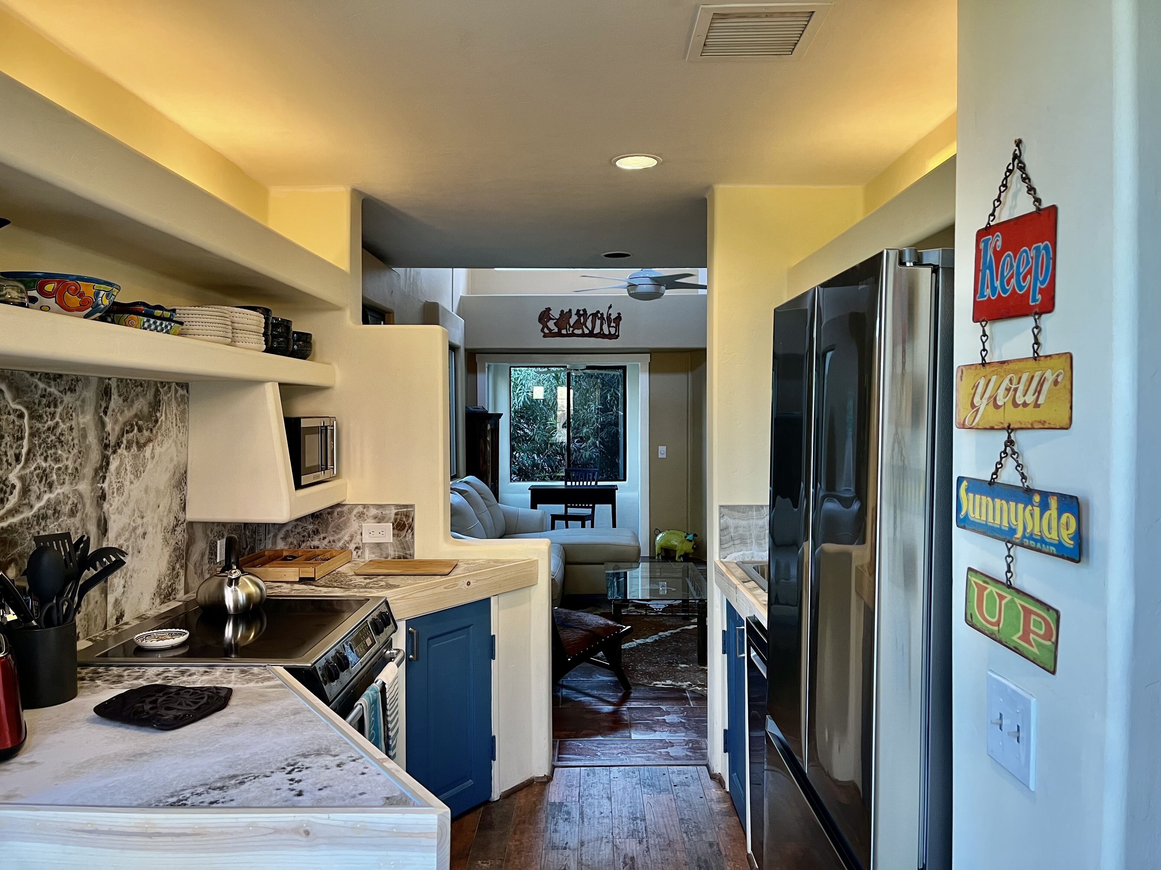 A modern kitchen with a marble countertop, stainless steel appliances, and a blue door leading to a dining area.