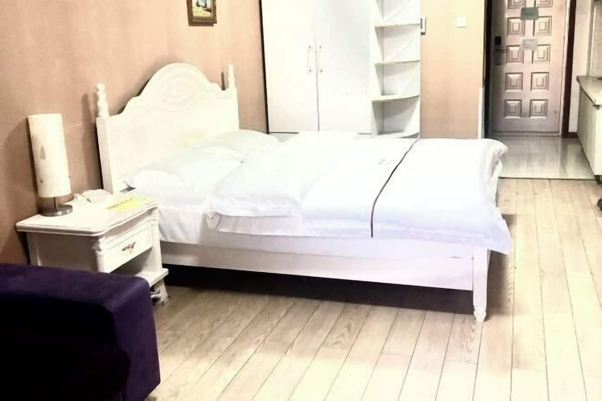 Ein Schlafzimmer mit einem weißen Bett, einem Nachttisch, einer Kommode und einer Tür.
