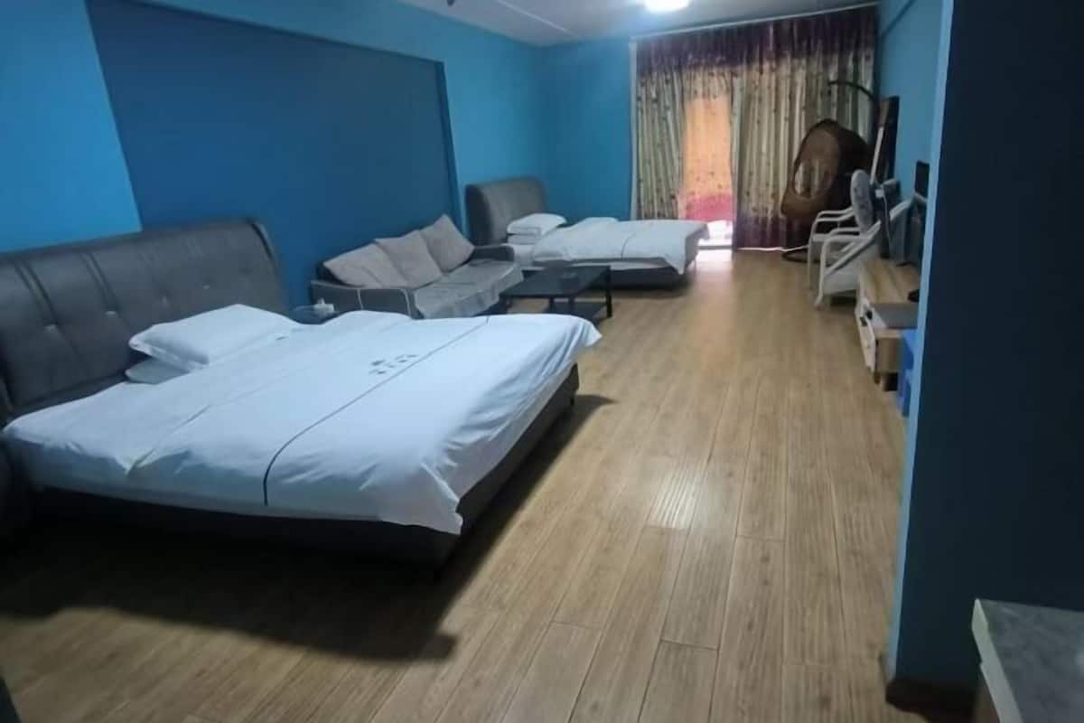 Ein Hotelzimmer mit drei Betten, Holzboden, blauer Wand und einem mit Vorhängen versehenen Fenster.