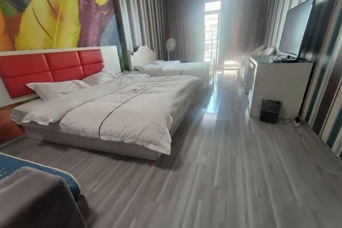 A hotel room with two beds, a desk, a chair, a TV, and a fan.