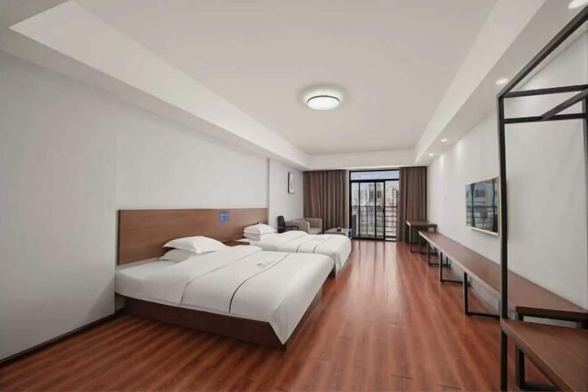 Ein Hotelzimmer mit Holzboden, zwei Betten, einem Schreibtisch und einem großen Fenster mit Blick auf die Stadt.