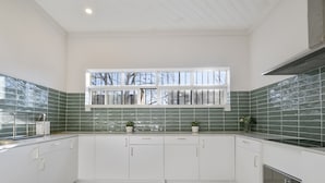 A modern kitchen with white cabinets, green backsplash tiles, and a window above the sink. - Urban Nomad Potts Point - 18-39 (Potts Point)