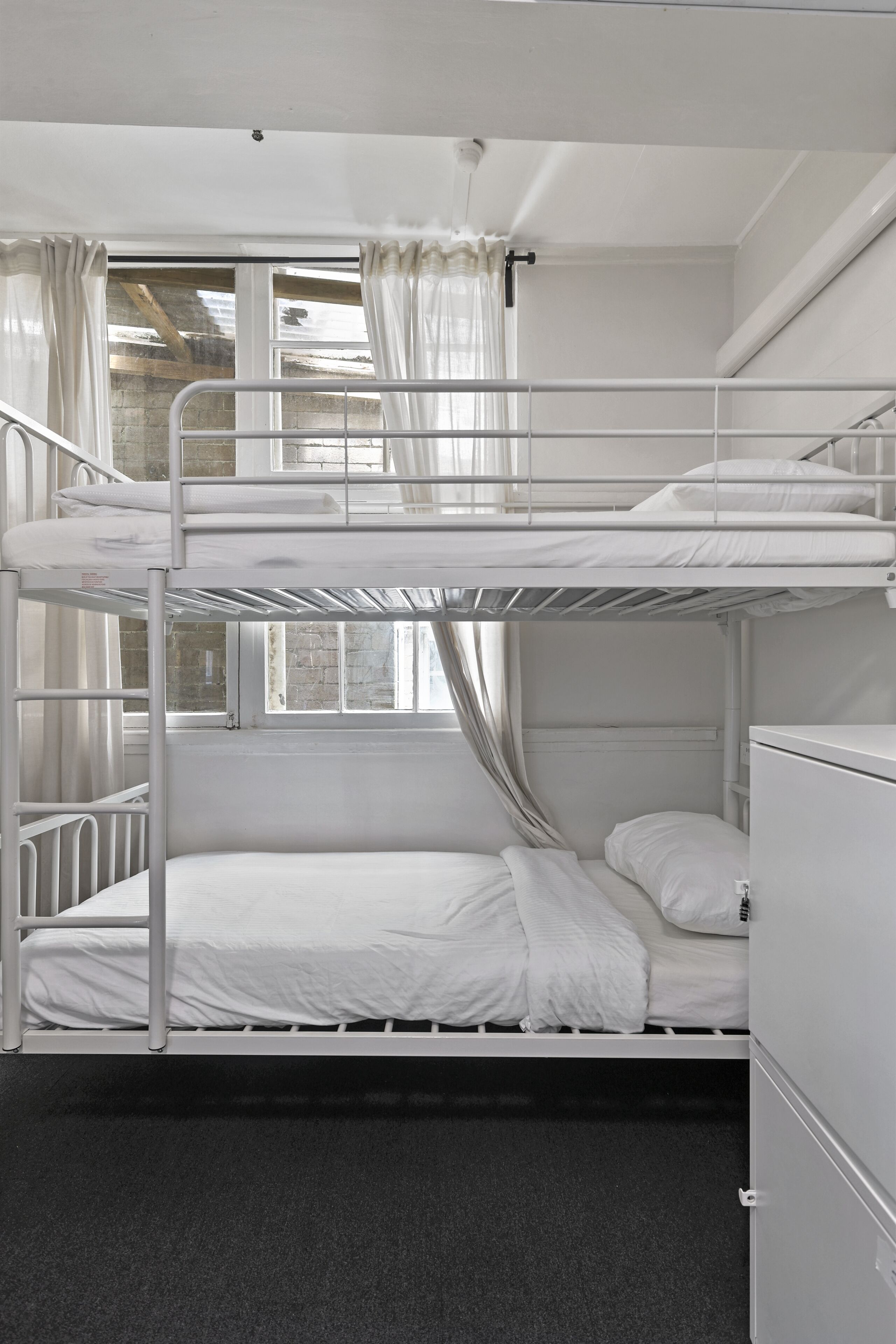 A bunk bed room with a window, curtains, and a radiator.