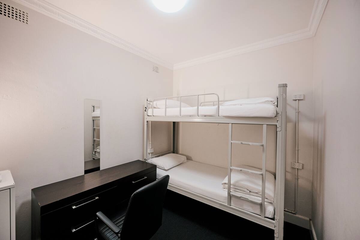 A bunk bed room with a desk and chair, a mirror, and a wardrobe.