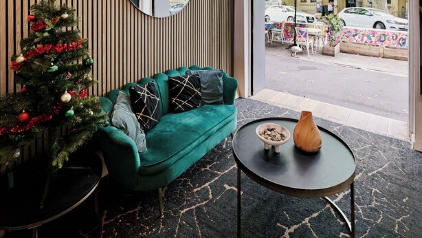 A hotel lobby with a Christmas tree, a teal sofa, a round table with a vase, and a large mirror reflecting the street view. - Urban Nomad Potts Point - 18-39 (Potts Point)