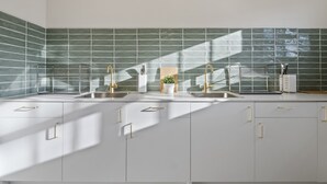 A modern kitchen with two sinks, a backsplash of green tiles, and a window casting shadows. - Urban Nomad Potts Point - 18-39 (Potts Point)