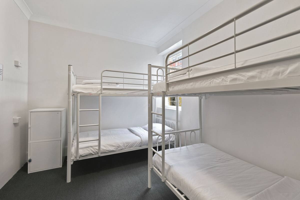 A bunk room with two beds, a small cabinet, and a window.