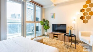 Quarto de hotel moderno com uma cama grande, televisão, planta e vista para a cidade.