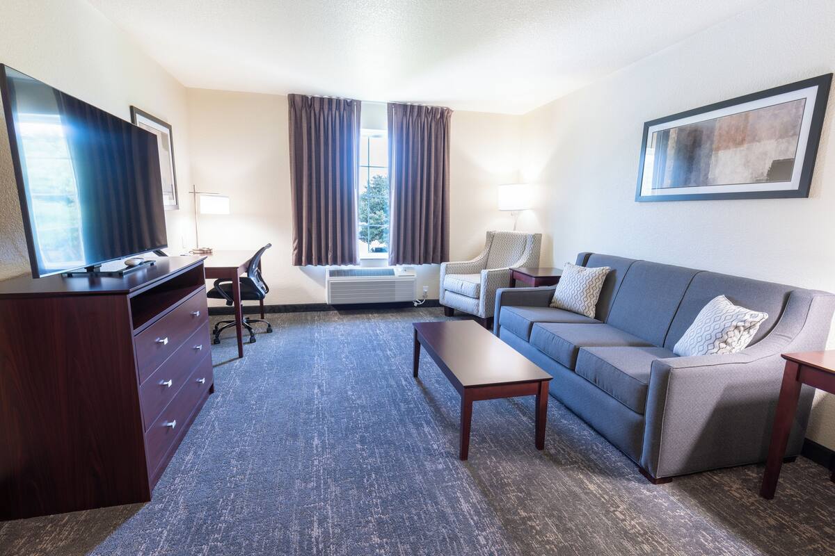 A hotel room with a flat-screen TV, a desk, a chair, a sofa, and a coffee table.