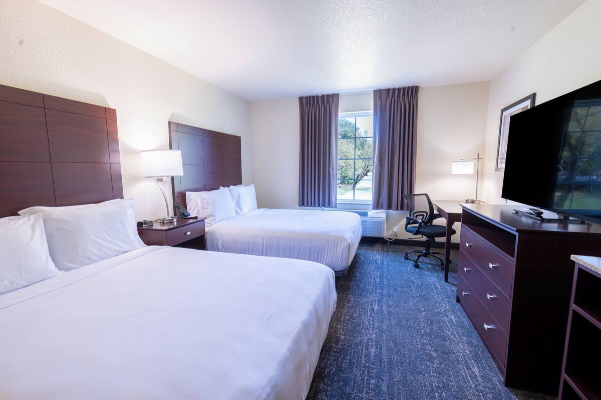 A hotel room with two beds, a desk, a chair, a TV, and a dresser.