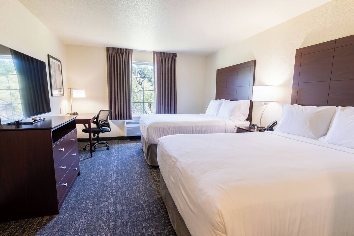 A hotel room with two beds, a desk, a chair, and a dresser.