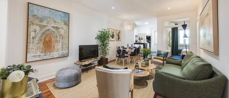 Una sala de estar moderna con un sofá verde, un sillón gris y una zona de comedor con una mesa y sillas.