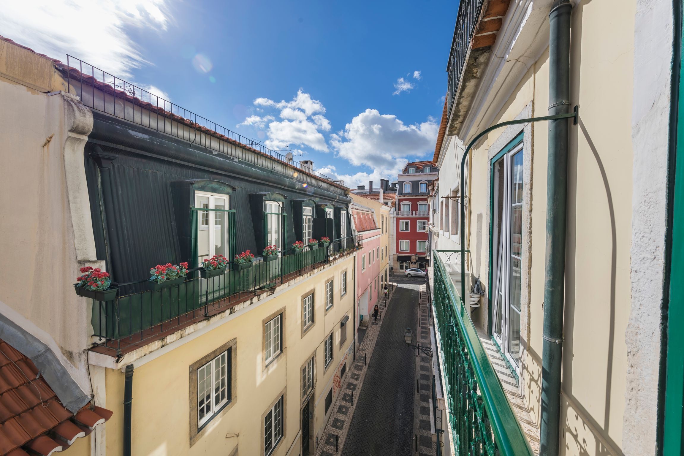 A narrow street between buildings with balconies, a cobblestone path, and a clear blue sky.