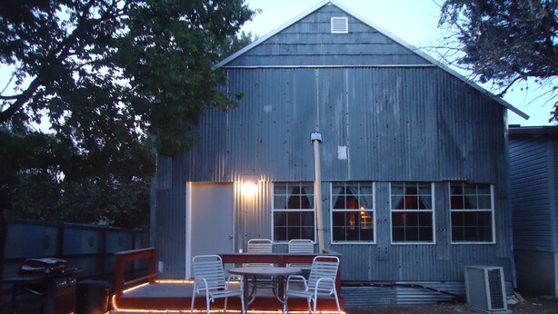 A rustic wooden building with a covered outdoor seating area featuring a table and chairs, illuminated by warm lights. - Nestled in Hill Country- Minutes from multiple attractions (Spring Branch)